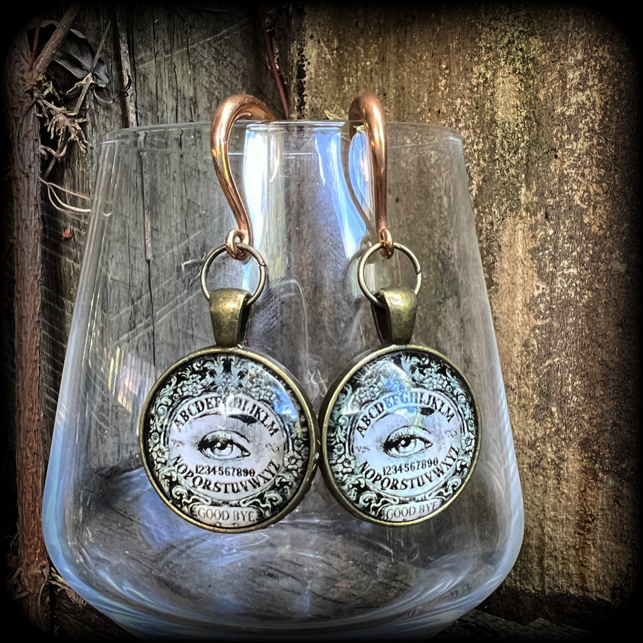 These gorgeous one of a kind Ouija board gauged earrings feature an antique bronze cabachon charm showing a classic ouija board image complete with the all seeing Mystic eye.

These earrings measure just on 6.5cms from tip to tip, and weigh approx 11 grams each.

This pair has been made on 6 gauge (4mm) stainless steel half curl hooks, suitable for stretched lobes.