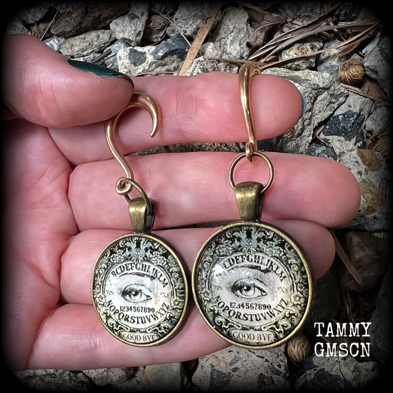 These gorgeous one of a kind Ouija board gauged earrings feature an antique bronze cabachon charm showing a classic ouija board image complete with the all seeing Mystic eye.

These earrings measure just on 6.5cms from tip to tip, and weigh approx 11 grams each.

This pair has been made on 6 gauge (4mm) stainless steel half curl hooks, suitable for stretched lobes.