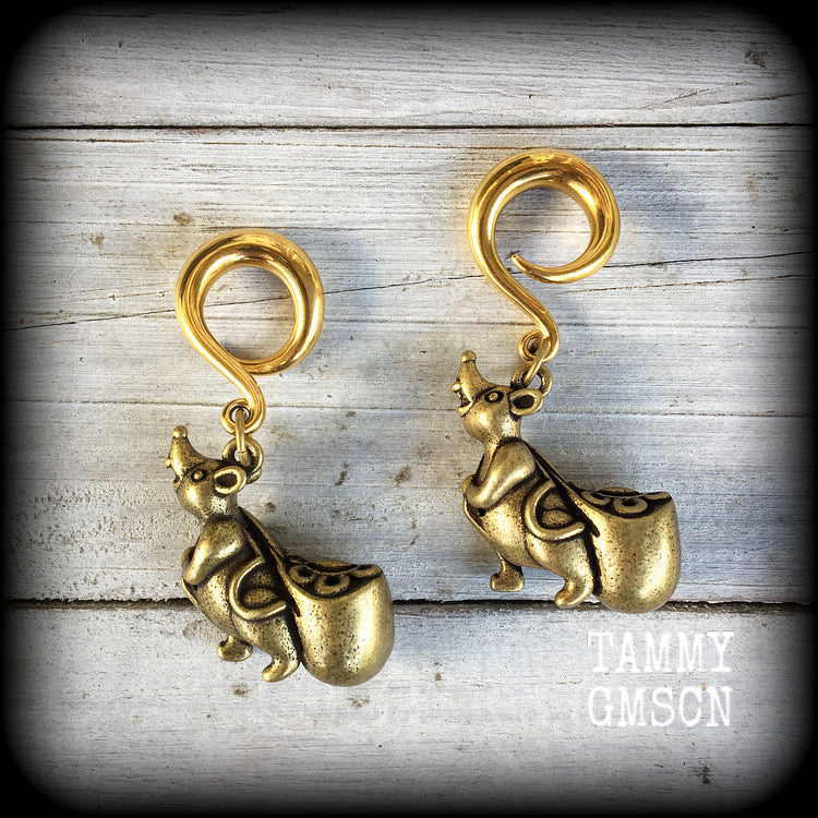 May include: Two gold-colored ear gauges with a dangling chinese money rat charm. Each rat charm is holding a small, round, gold-colored bag. The text 'TAMMY GMSCN' is visible at the bottom of the image.