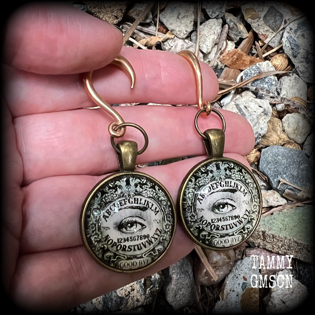 These gorgeous one of a kind Ouija board gauged earrings feature an antique bronze cabachon charm showing a classic ouija board image complete with the all seeing Mystic eye.

These earrings measure just on 6.5cms from tip to tip, and weigh approx 11 grams each.

This pair has been made on 6 gauge (4mm) stainless steel half curl hooks, suitable for stretched lobes.
