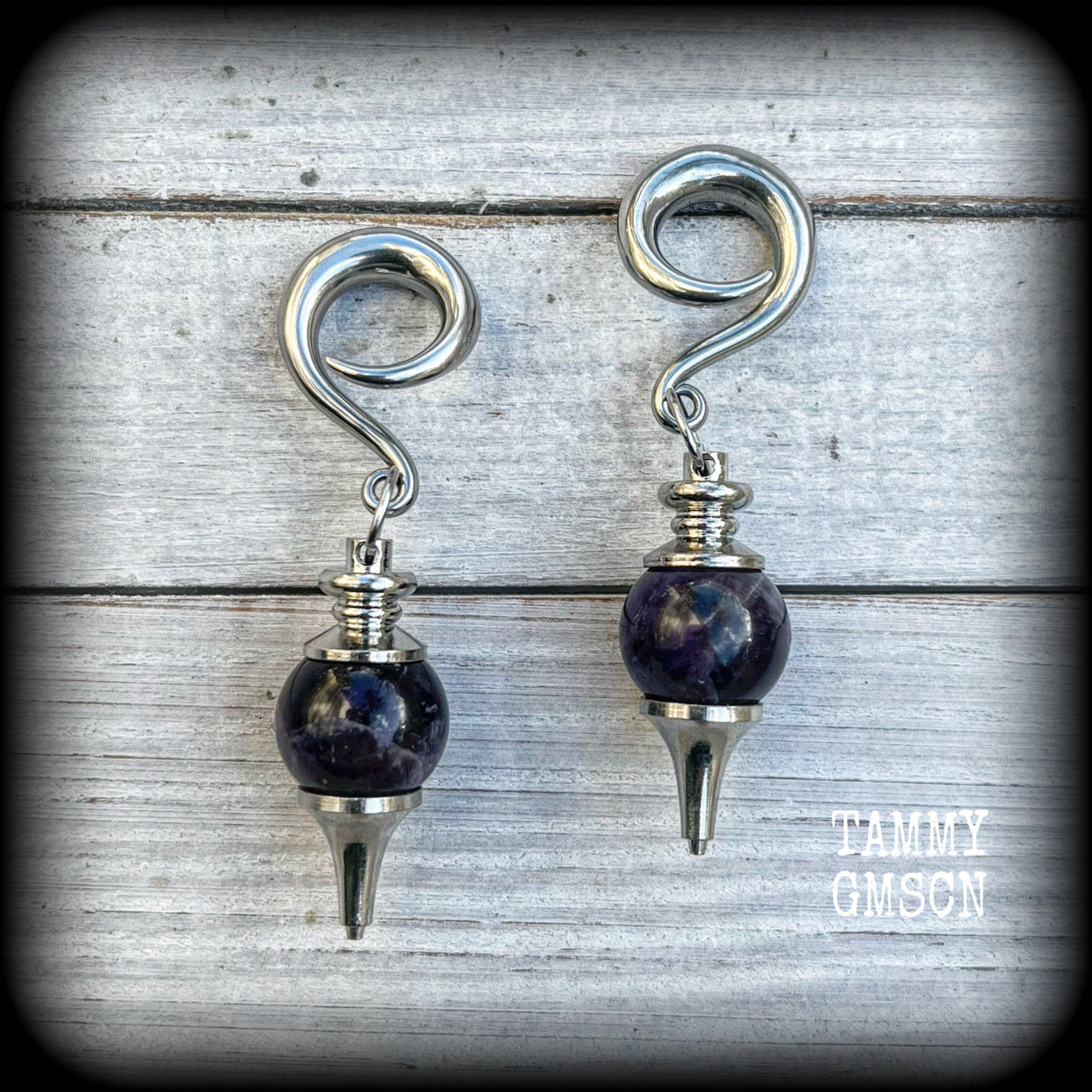 Featuring a pair of beautiful plump purple amethyst pendulums, this pair of earrings weighs approx 21 grams a piece and measure just over 7cms from tip to tip.
This pair have been made on 2 gauge (6mm) surgical steel full curl hooks, to be worn in stretched lobes.