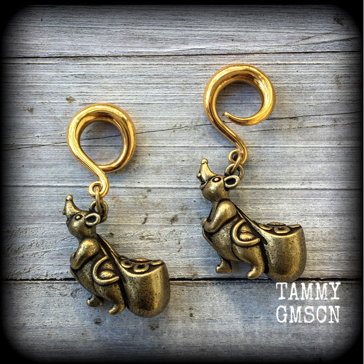 May include: Two gold-colored ear gauges with a dangling chinese money rat charm. Each rat charm is holding a small, round, gold-colored bag. The text 'TAMMY GMSCN' is visible at the bottom of the image.