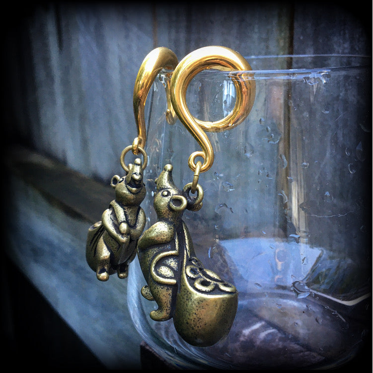 May include: Two gold-colored ear gauges with a dangling chinese money rat charm. Each rat charm is holding a small, round, gold-colored bag. The text 'TAMMY GMSCN' is visible at the bottom of the image.